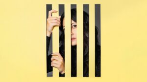A women stands behind yellow bars in a promotional image for English Touring Opera's Manon Lescaut.