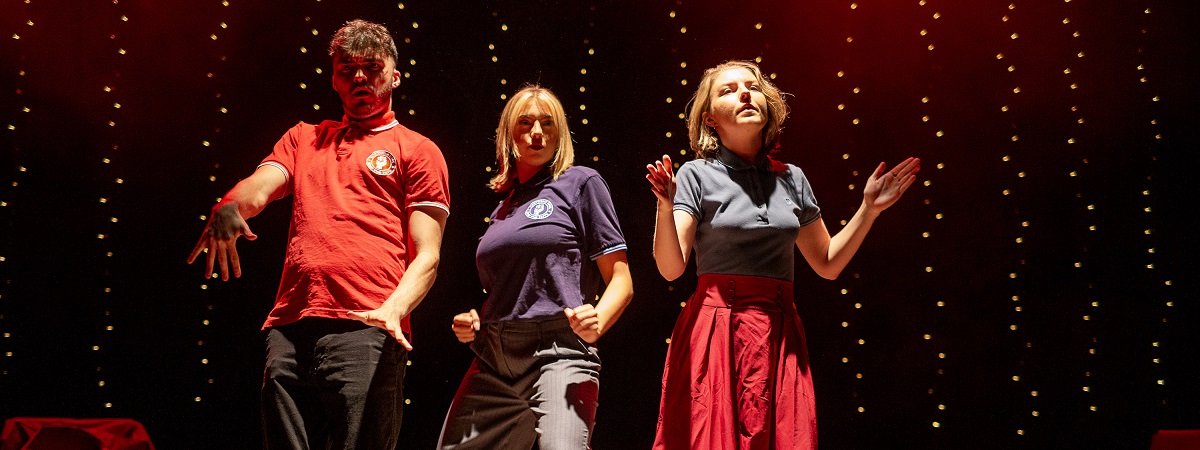 Three people wearing tops with a 'Northern Soul - Keep The Faith' logo dance in a production shot from John Godber's Do I Love You?