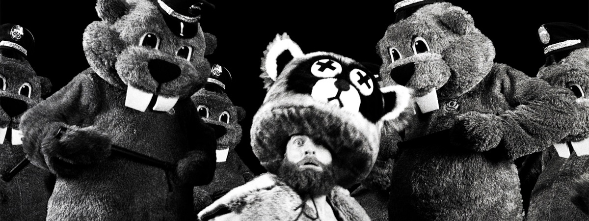 A man, dressed in a racoon outfit, is surrounded by people dressed as beavers in a still from Hundreds of Beavers