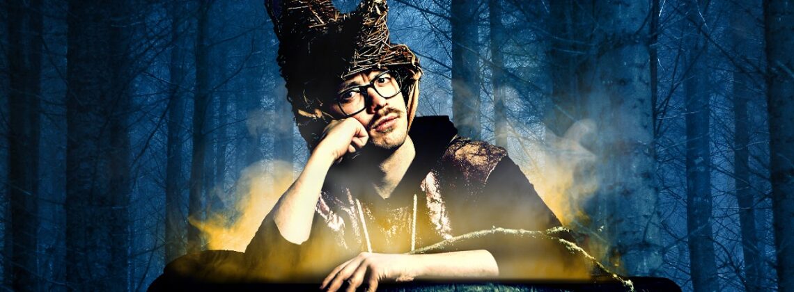Edy Hurst sits in a cauldron wearing a witch's hat with trees in the background.