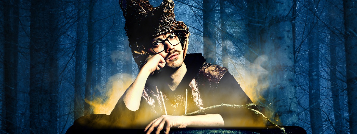 Edy Hurst sits in a cauldron wearing a witch's hat with trees in the background.