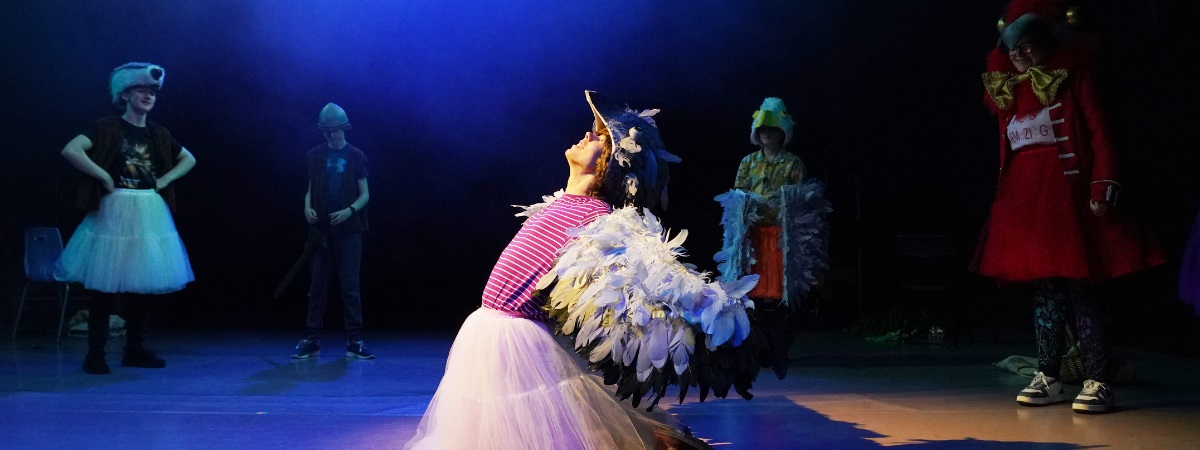 A young performer kneels as other performers watch on in an image for Gala Youth Theatre.