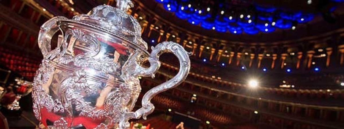 A trophy stands in front of an auditorium in a promotional image for The North of England Brass Band Championships.