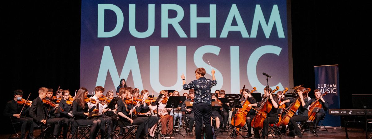 A photograph of a group of young people playing music in front of a screen which reads 'Durham Music'.