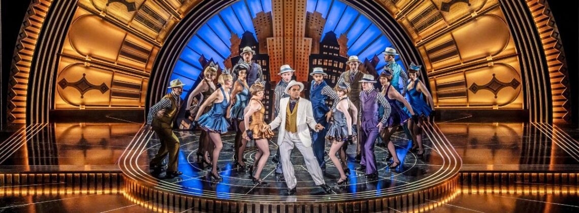Cast members perform on stage in a still from Top Hat the Musical.