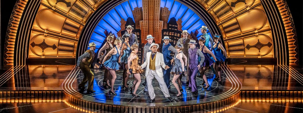 Cast members perform on stage in a still from Top Hat the Musical.