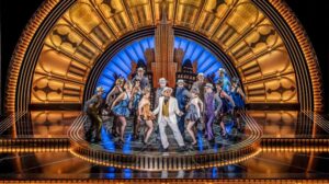 Cast members perform on stage in a still from Top Hat the Musical.